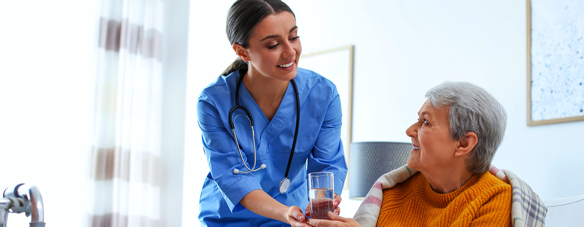 A nurse giving water to an elderly woman