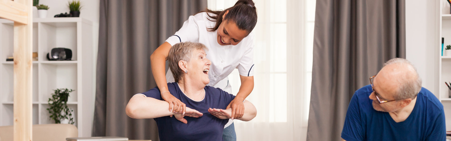A nurse holding the arm of an elderly woman while an elderly man looking at them